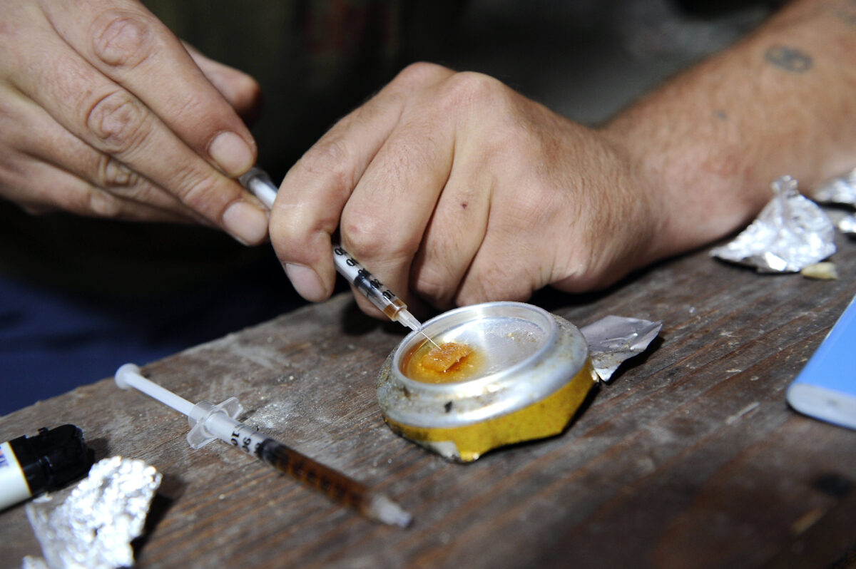 Addict using the bottom of a soda can to liquify heroin and suck it into a syringe for use.