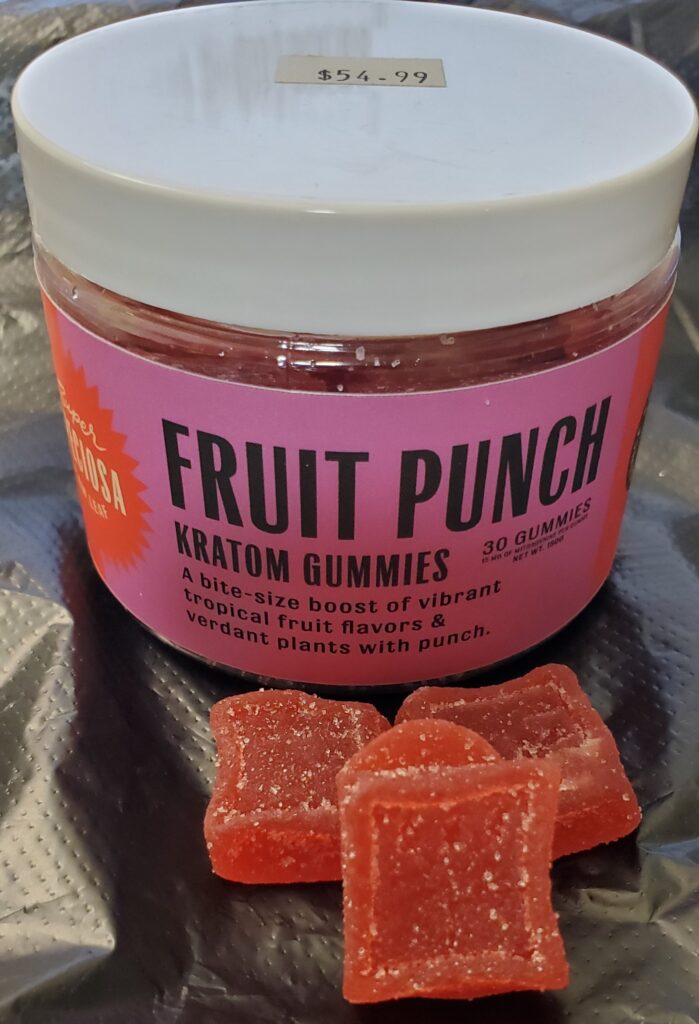 Image is small plastic jar with white lids and pink label around it. In front of the jar are 3 red gummy squares with some sugar like substance sprinkled on them. The writing on label says FRUIT PUNCH with Kratom Gummies under it. Below that is "A bite sized boost of tropical fruit flavors and verdant plans with punch." On top of the white lid is a small price tag that say $54.99.