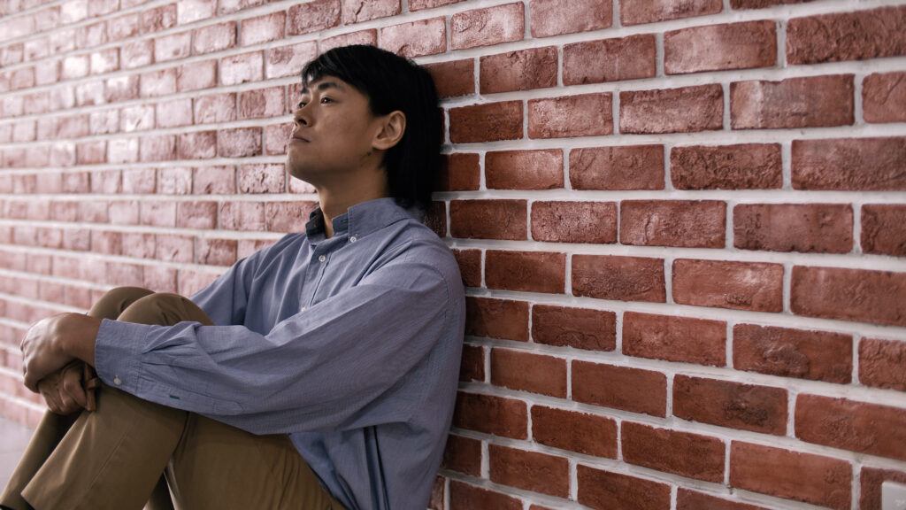 Young man sitting against a wall looking depressed. He represents the sadness people might feel because of the fentanyl crisis.